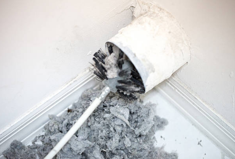 a very dusty dryer vent with a brush partially inside of it